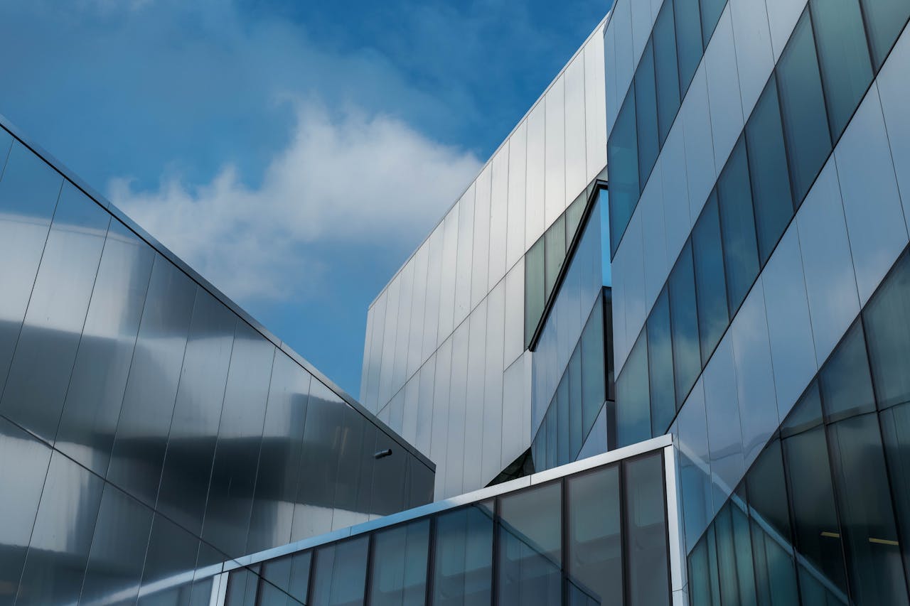 Low angle view of modern glass buildings reflecting blue sky and clouds.
